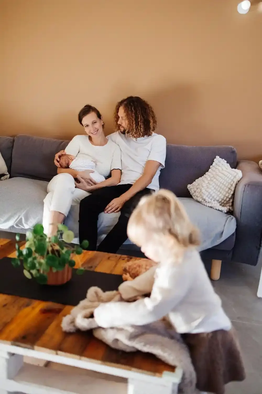 Les parents sur le canapé avec le nouveau-né pendant que la grande sœur joue avec sa poupée sur la table basse
