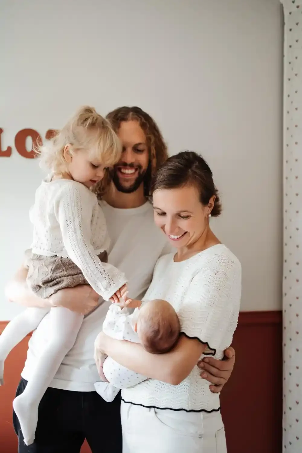 Parents debout enlacés autour de leur nouveau-né et de leur fille de 2 ans, portrait de famille lifestyle à domicile