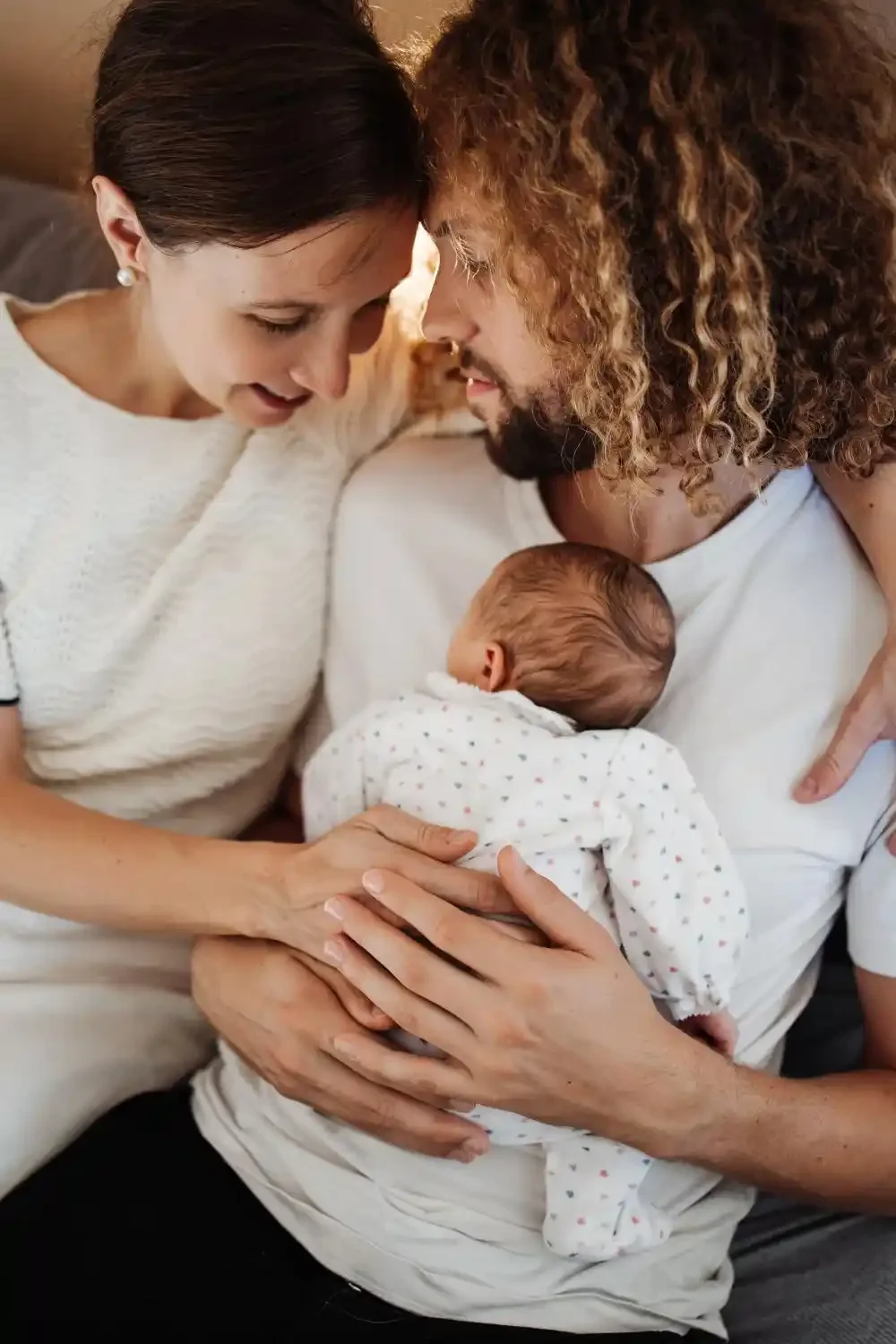 Les parents penchent la tête vers leur nouveau-né pour le regarder dormir, souvenir de naissance à Villeneuve-d’Ascq