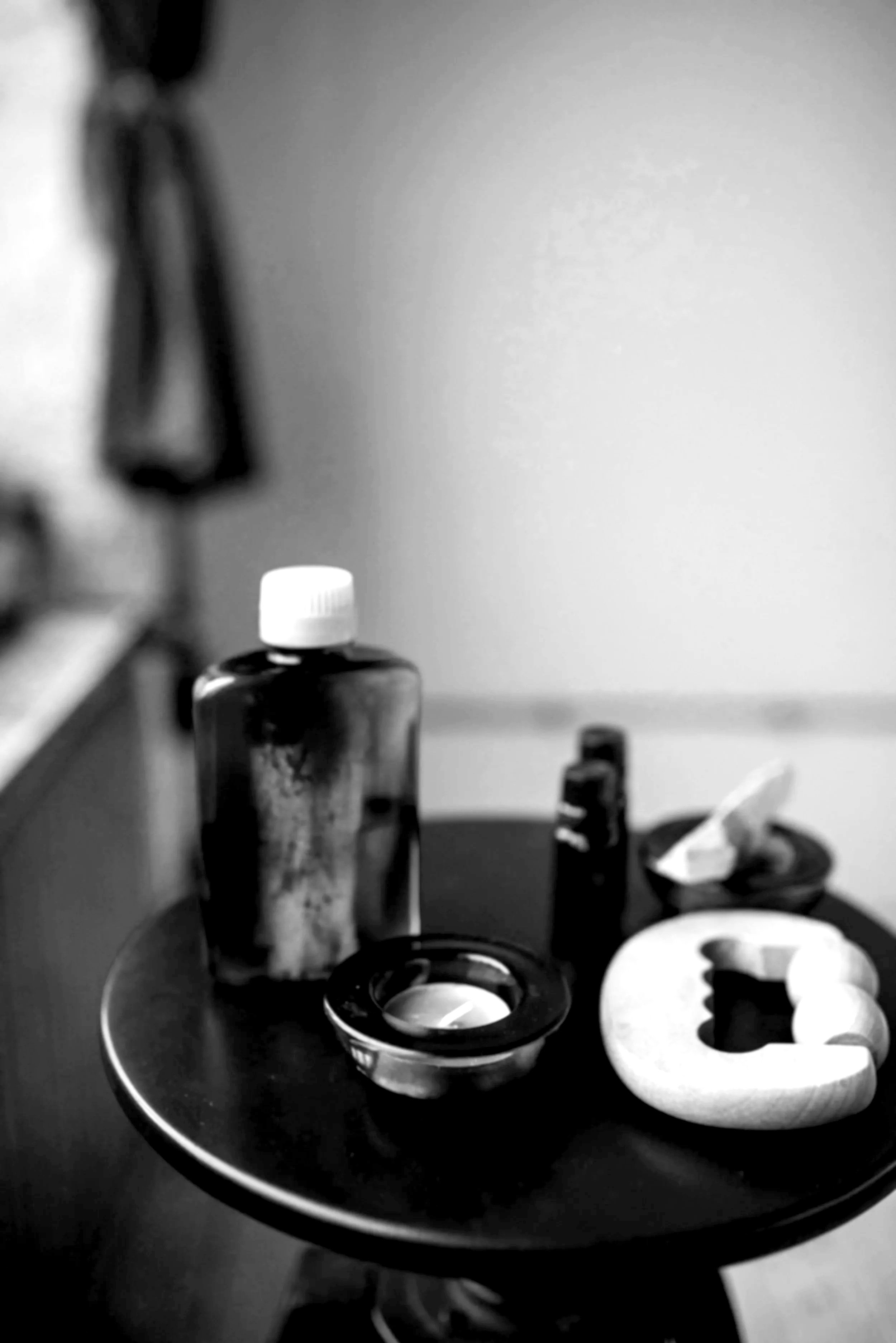 A black and white photo of a tabletop with various cosmetic or skincare bottles, jars, and a small bowl.