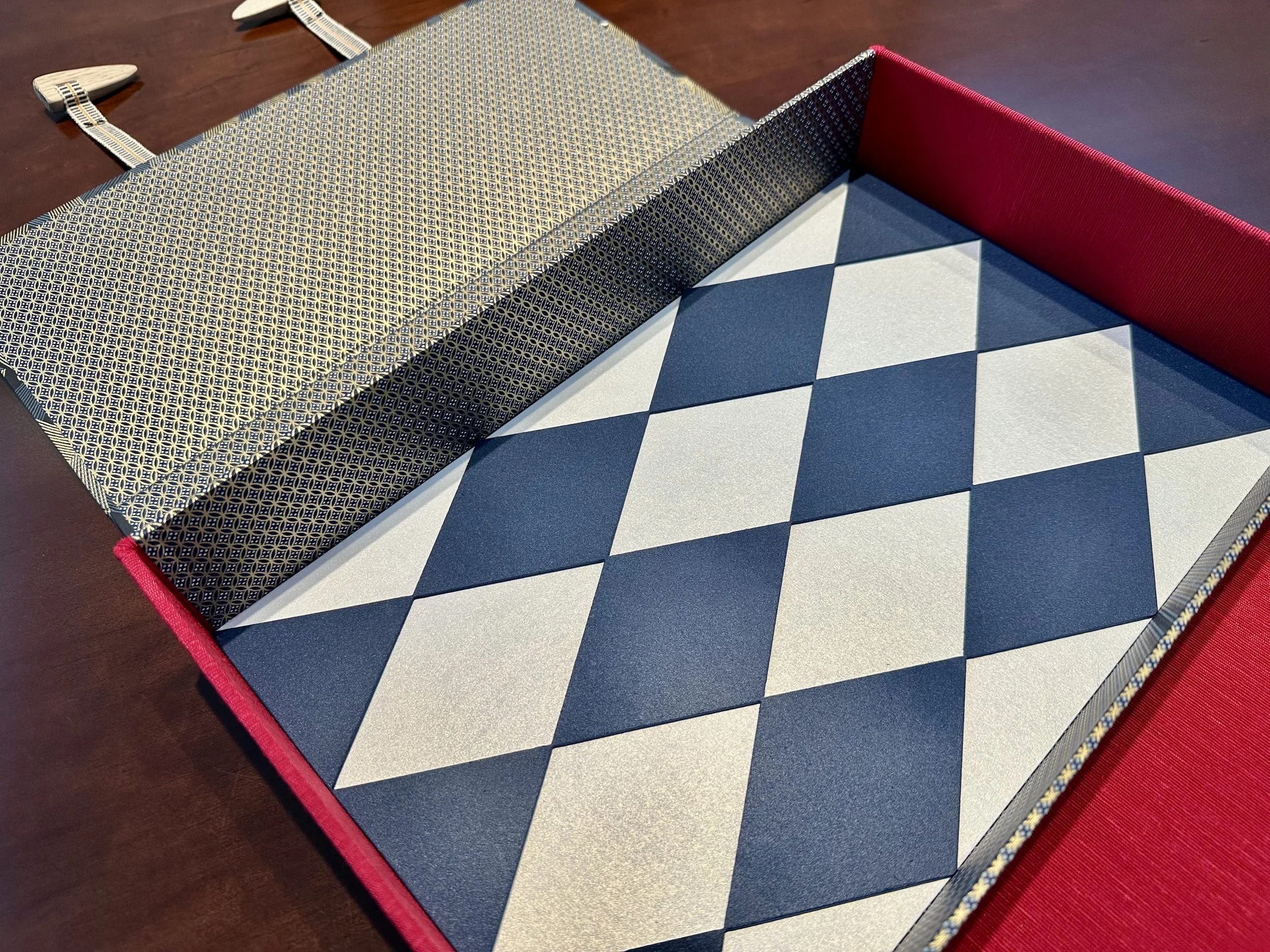 A chessboard with black and white squares, with a red border along the edge. The chess pieces are not visible in the image. The game setup is visible on a dark brown table.