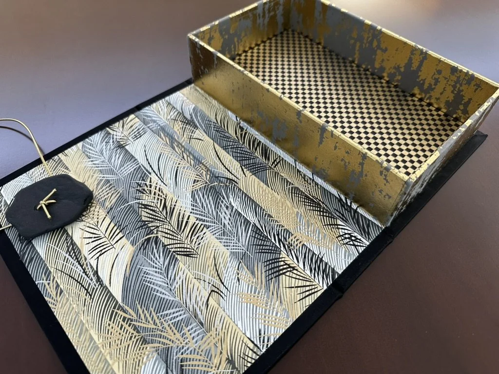 Decorative jewelry display box with patterned interior and textured gold accents, containing earrings and necklaces