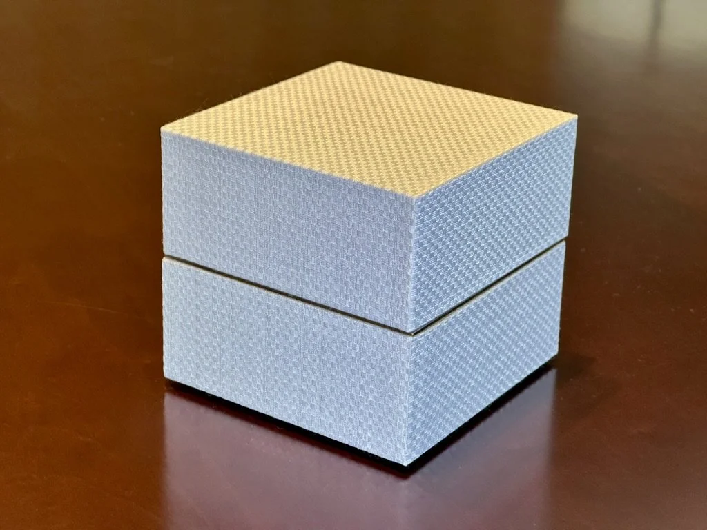 A small, light blue, textured cube-shaped box with a separate lid on top, placed on a dark wooden surface.