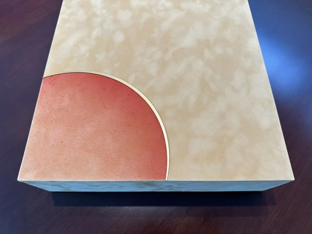 A beige cardboard box with a semi-circular red design on the corner, placed on a dark wooden surface.