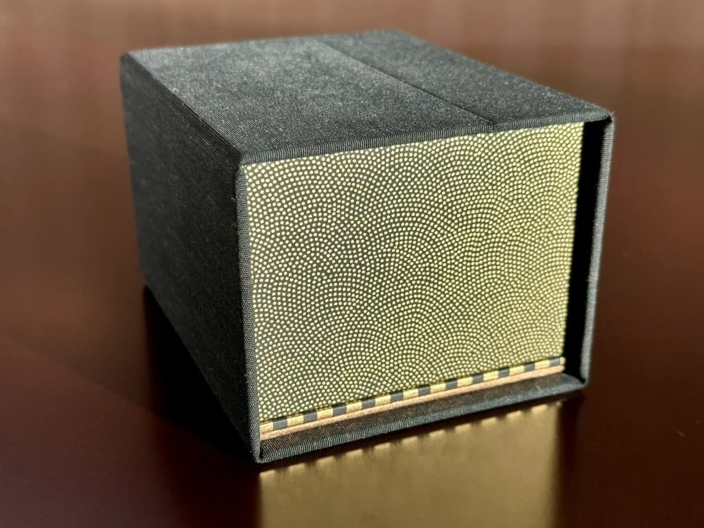 A black textured cube-shaped box sitting on a wooden surface.