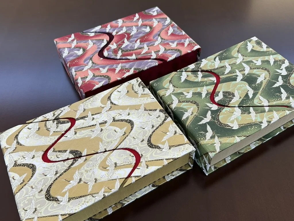 Three decorated gift boxes with colorful patterns and white bird motifs, placed on a dark surface.