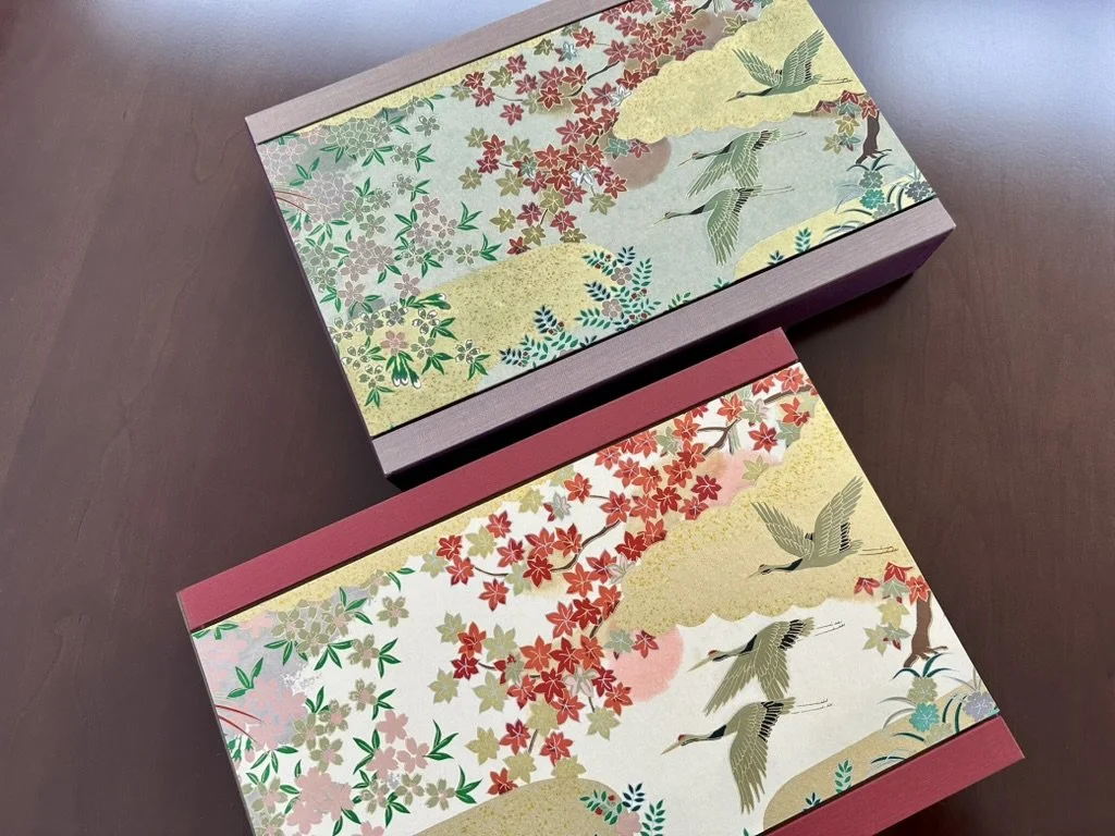 Two decorative boxes with Japanese-inspired landscape designs featuring cranes, cherry blossoms, and trees in pastel colors.