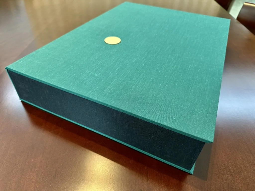 A closed teal-colored box with a gold circular sticker on top, placed on a wooden surface.