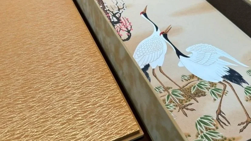 Close-up of a traditional Asian painting featuring two cranes standing among green foliage with a background of blossoms.