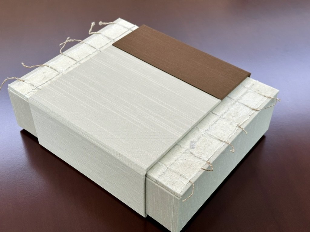 Stack of white tiles on paper with brown tile on top, tied with string on a dark surface.