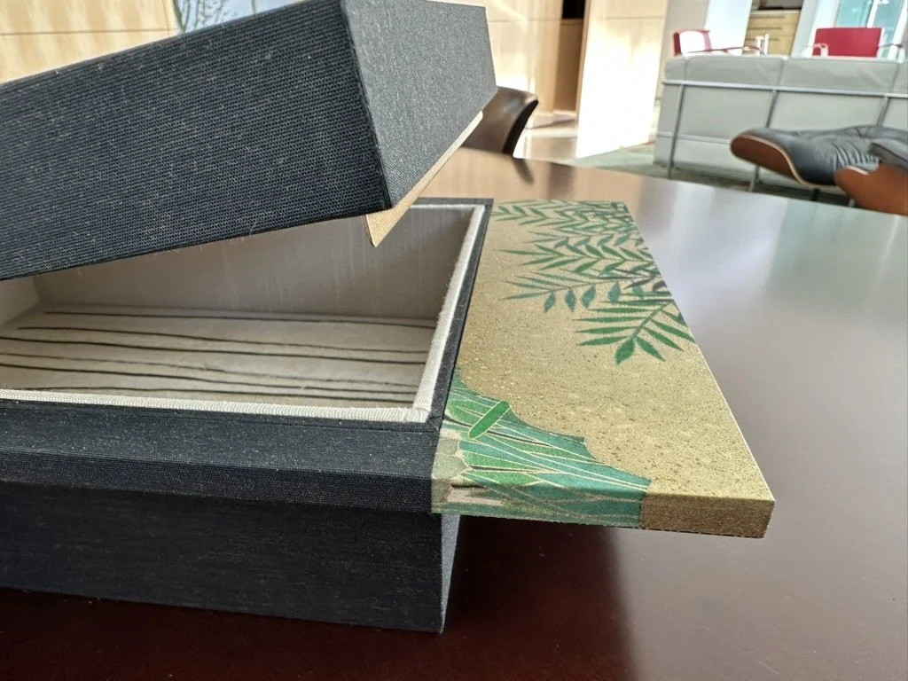 Open decorative box with tropical-themed lid and empty striped interior on table in room with furniture.
