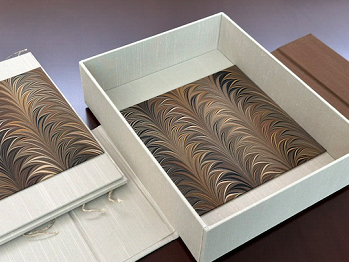 Open white box with marbled paper lining, next to matching marbled paper on a folder or box lid.