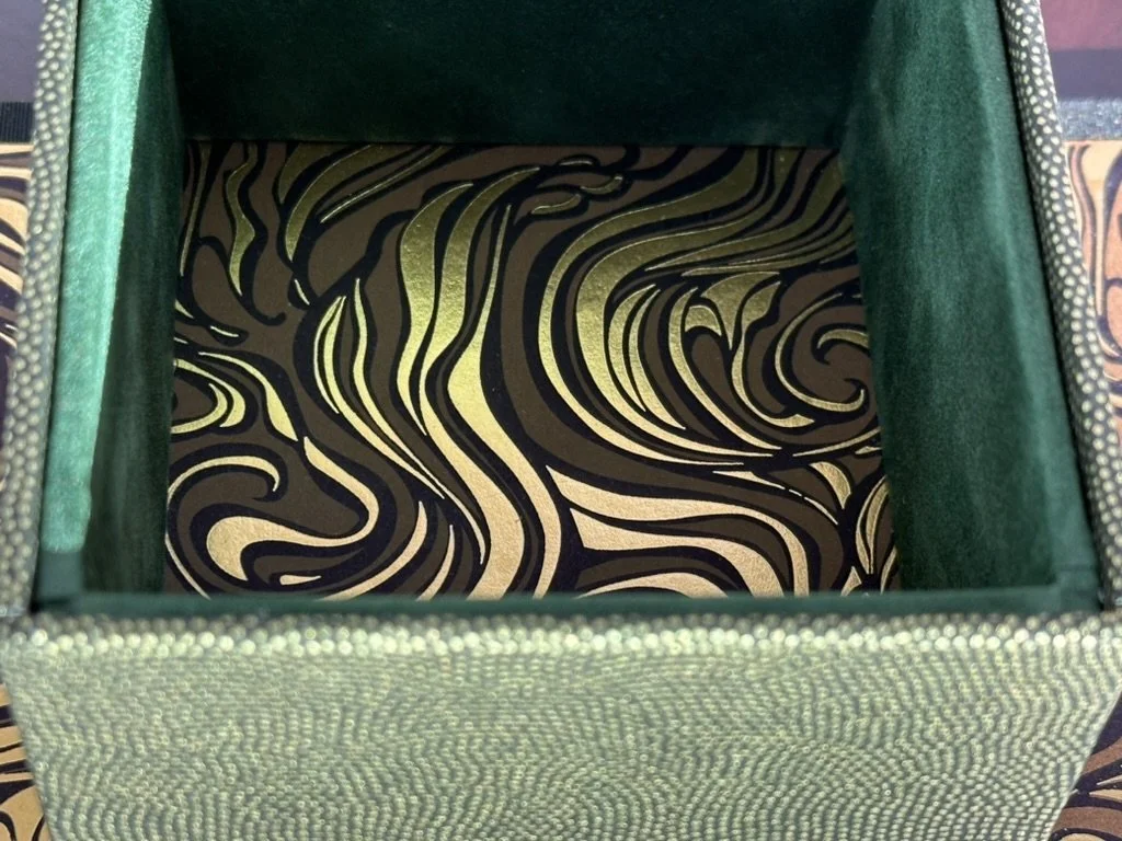 Open green textured box with black and gold swirling patterned interior.