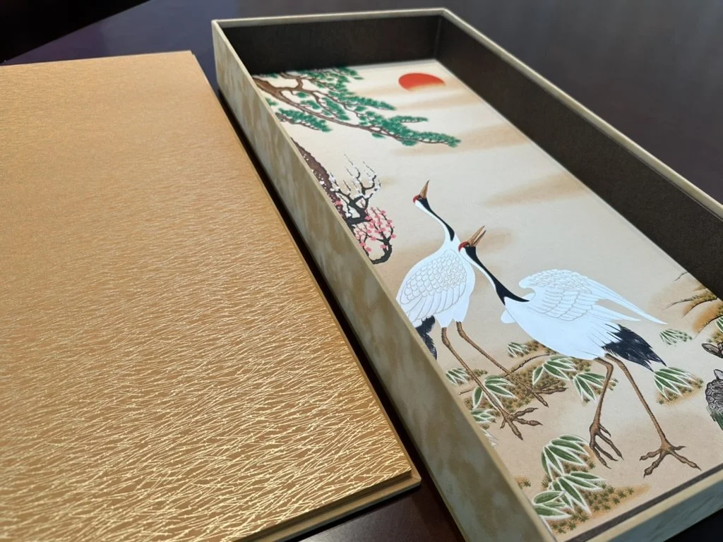 A decorative box with a traditional Japanese-style painting of two cranes, trees, and a red sun inside.