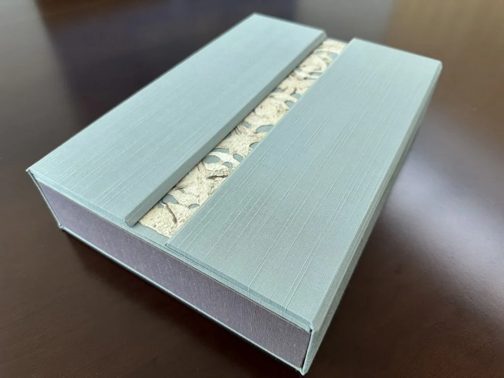Decorative tissue box with a blue textured lid and intricate beige-patterned tissue inside, placed on a brown surface.