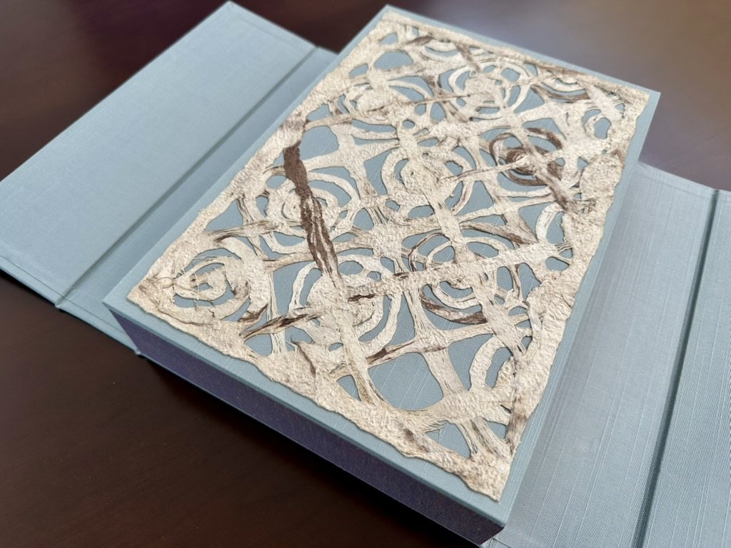 Blue presentation folder with a decorative, intricate cut-out metal or paper overlay on top.