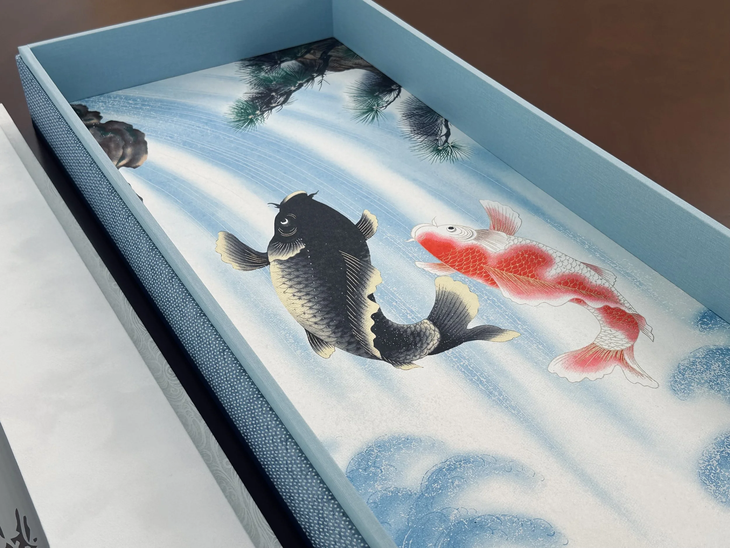 A decorative tray featuring an illustration of two colorful koi fish swimming in water, with green foliage and a flowing water background.