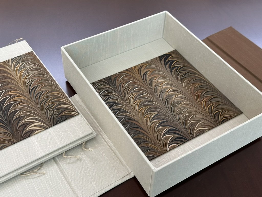 A box with marbled paper and a matching booklet on a dark surface.