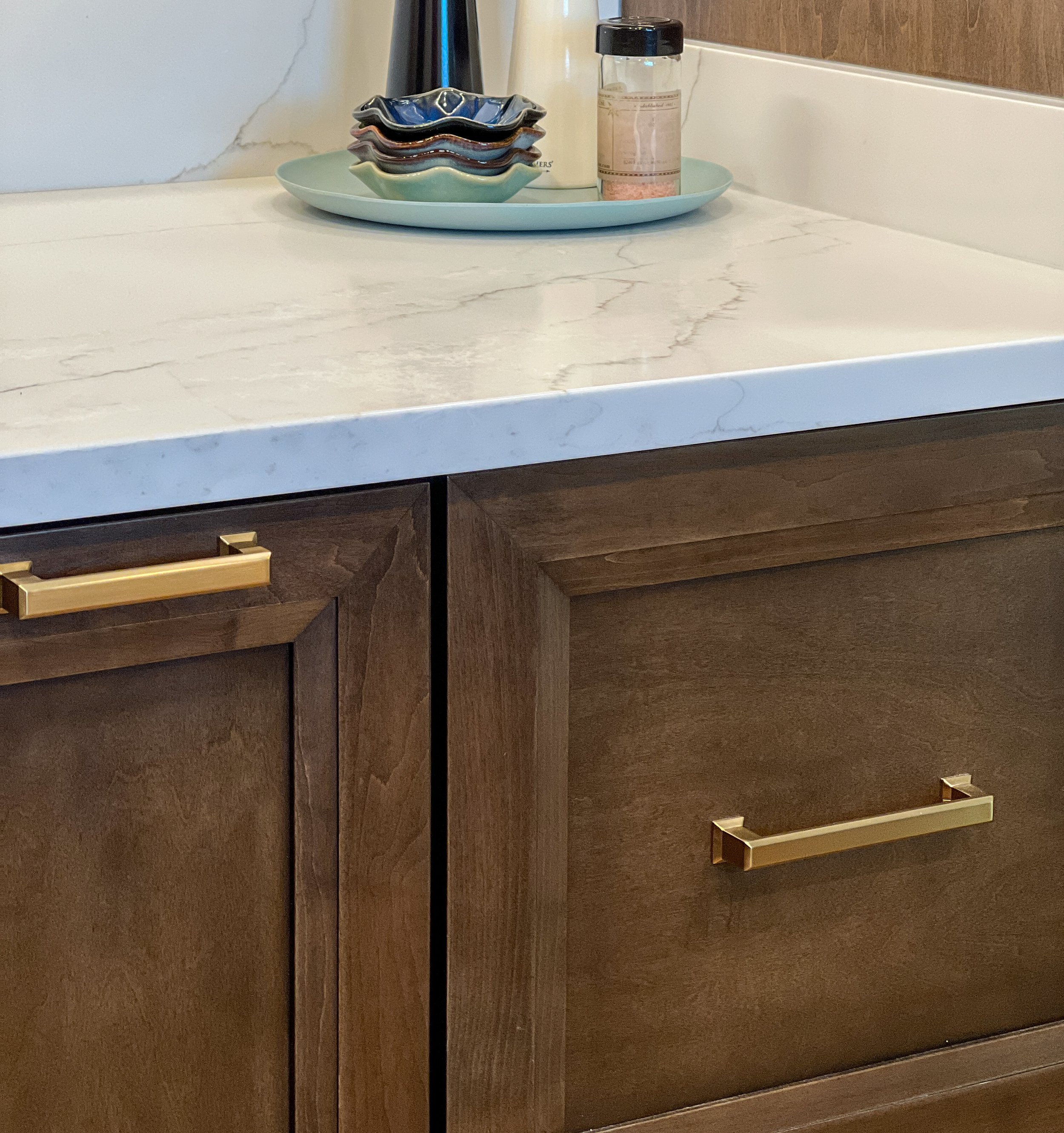 Close-up of rich brown stained wood cabinets with modern brushed gold handles, topped with a white marbled quartz countertop.