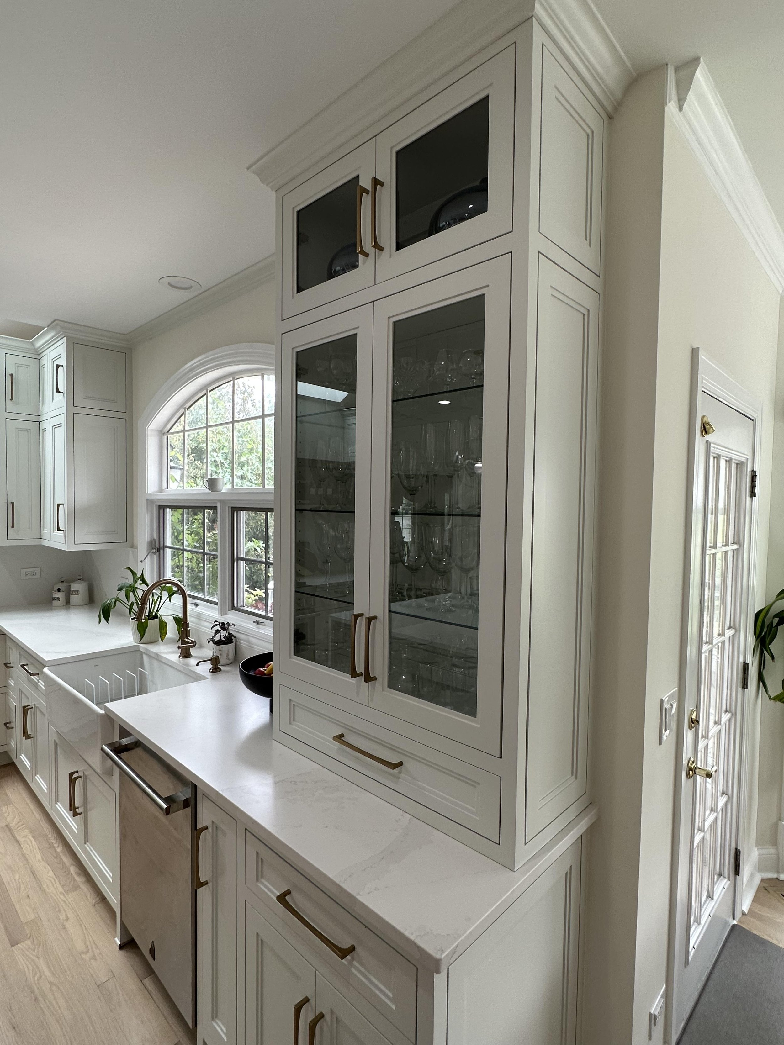 In this captivating image, a countertop cabinet with glass inserts takes center stage, artfully displaying an array of beautiful dishes and glasses. A harmonious blend of functionality and visual appeal, enhancing the kitchen with curated elegance.