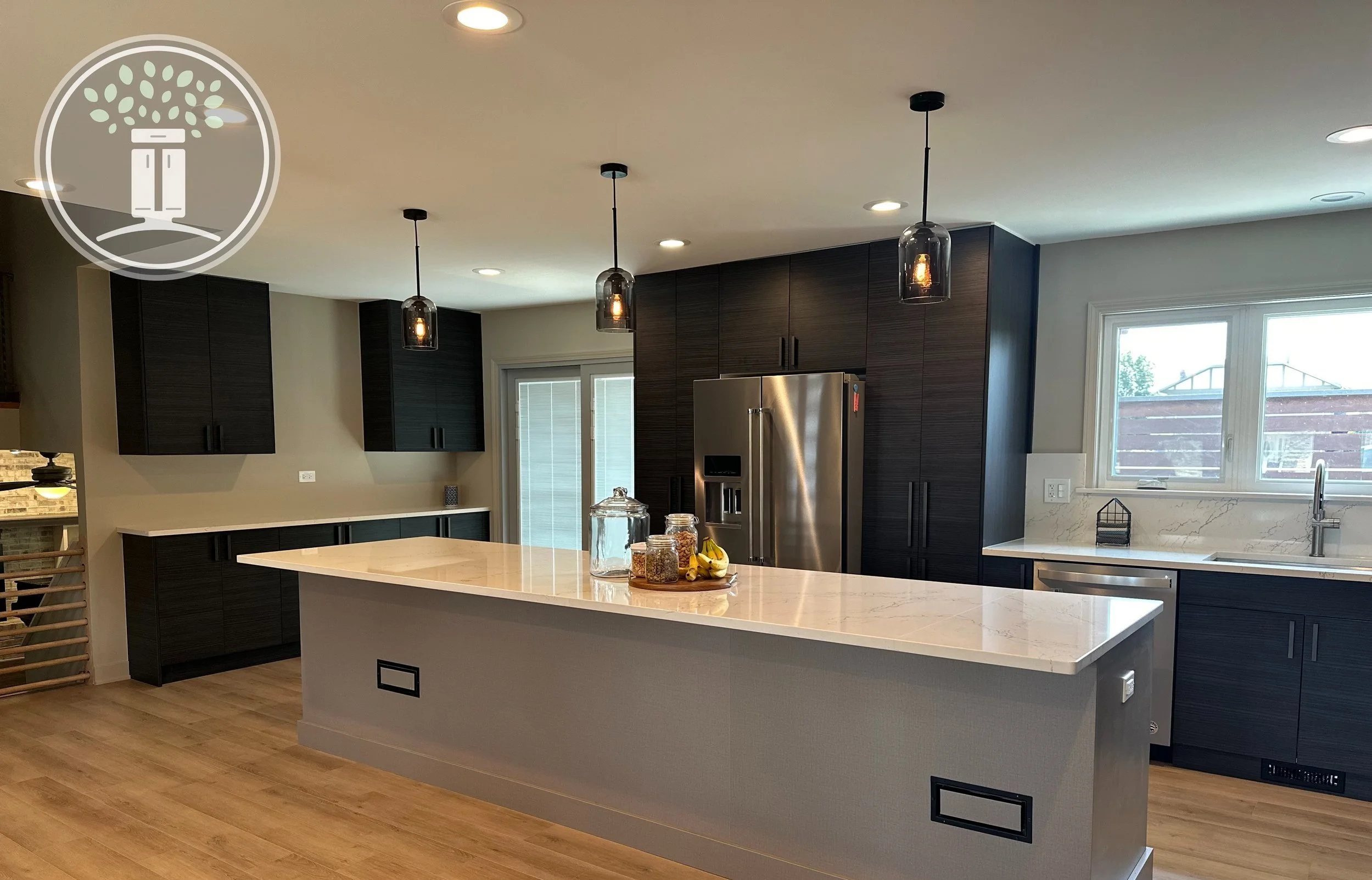 Modern kitchen with pendant lighting, dark cabinetry, marble island, stainless steel appliances, and wooden flooring.