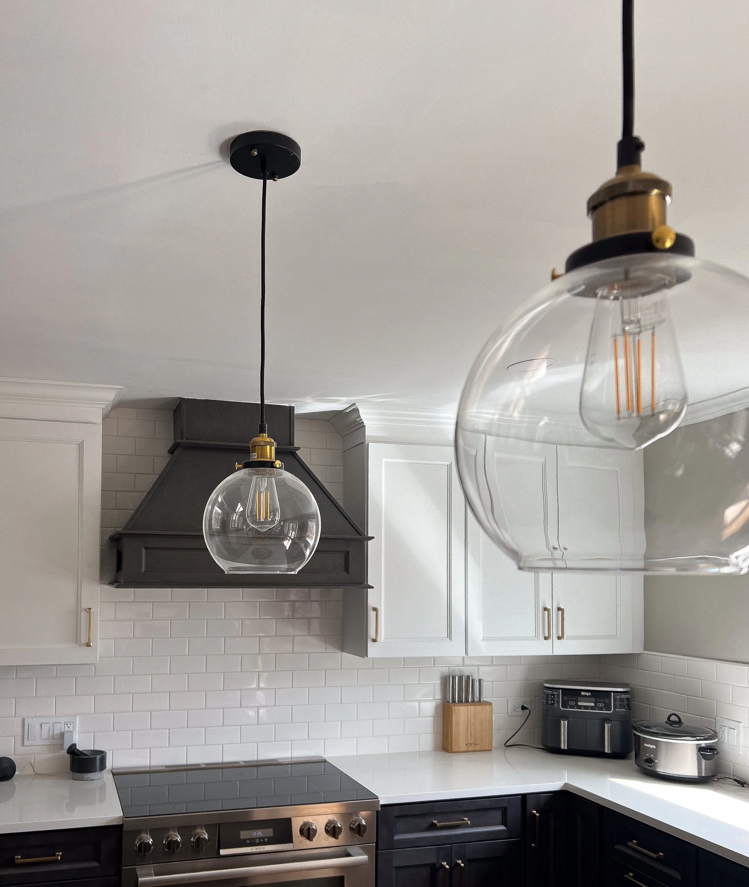 Modern kitchen with white cabinets, black handles, stainless steel appliances, and globe pendant lights.