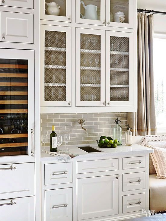 Modern kitchen with white cabinets, glass cabinet doors, wine fridge, and countertop with lime-filled bowl and wine bottle.