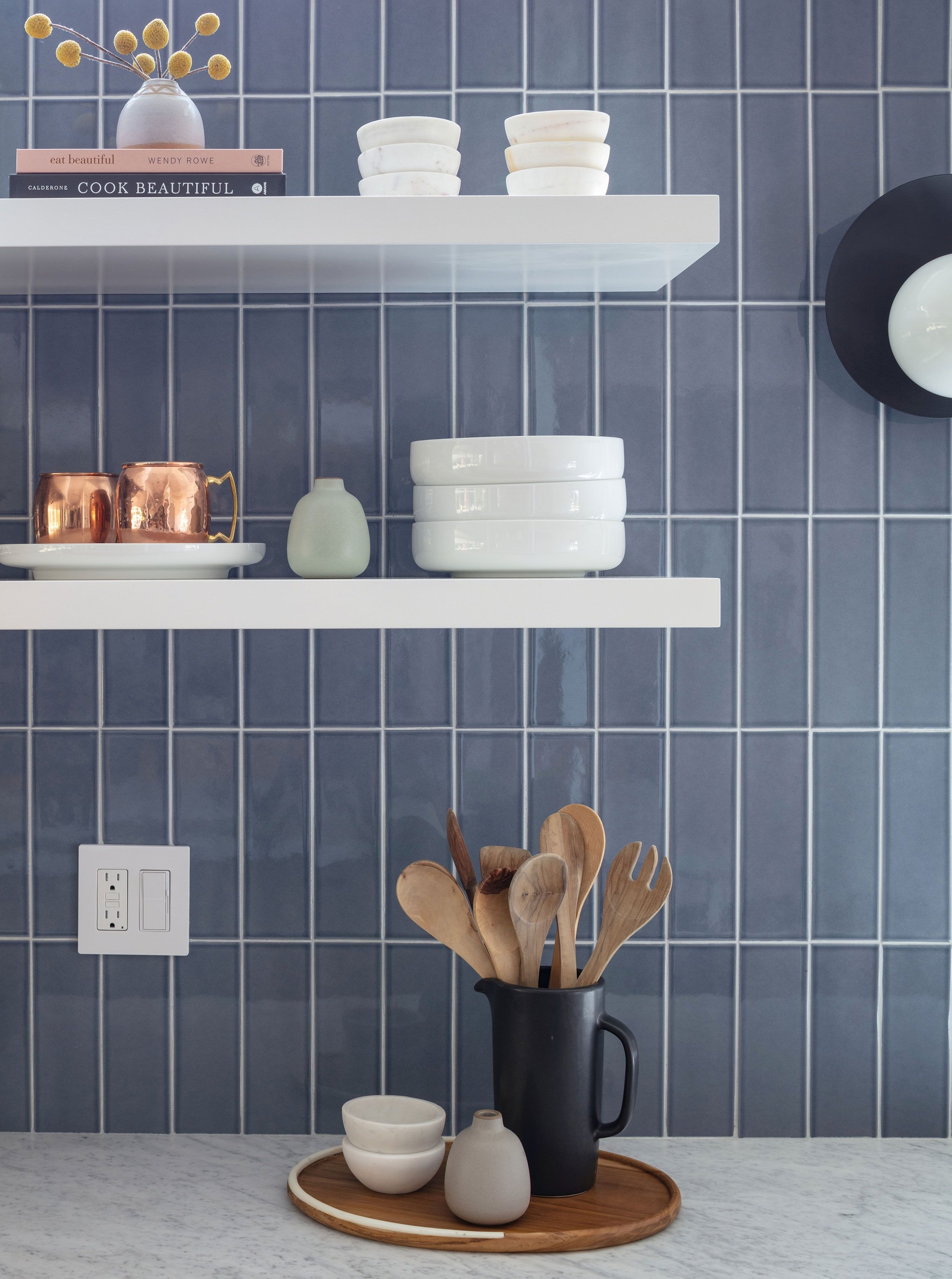 In this image, a kitchen boasts a striking blue vertical stacked tile backsplash with white grout, creating a visually dynamic and modern aesthetic that adds depth and character to the space.