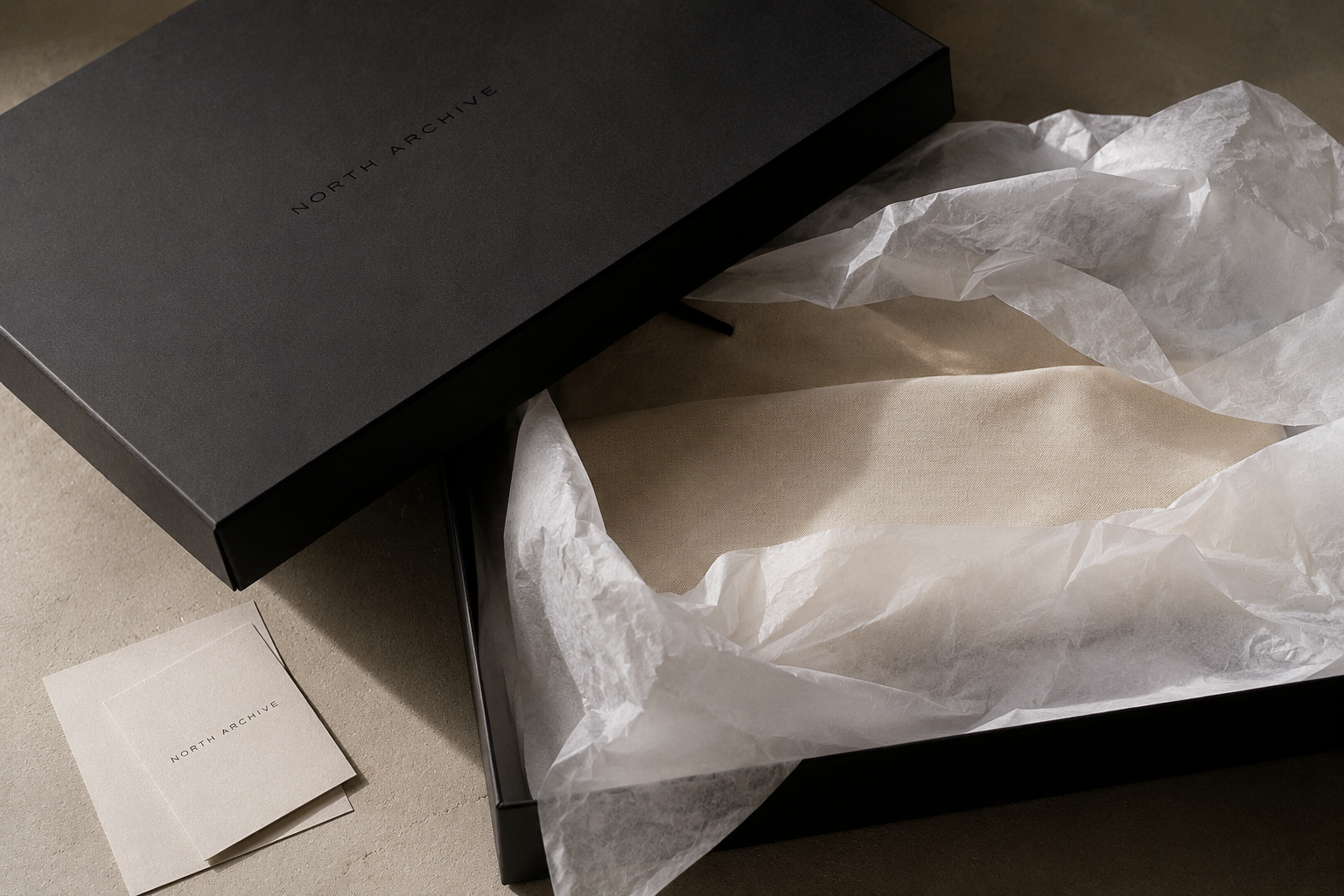 A black box labeled 'North Archive' with white tissue paper inside, and a small card with 'North Archive' printed on it next to the box.