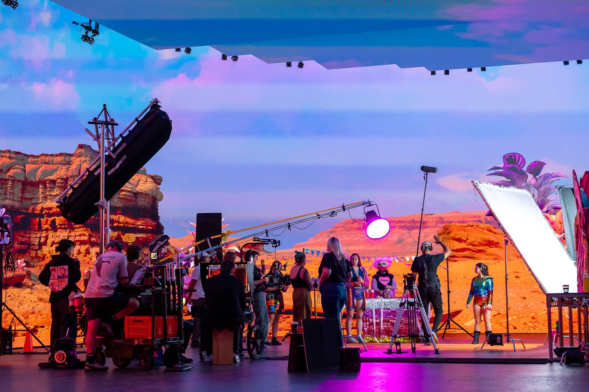 Behind-the-scenes on Killjoy in a virtual production studio. Crew members are working with cameras, lighting, and equipment, with a virtual backdrop resembling a desert terrain canyon landscape and a purple sky.