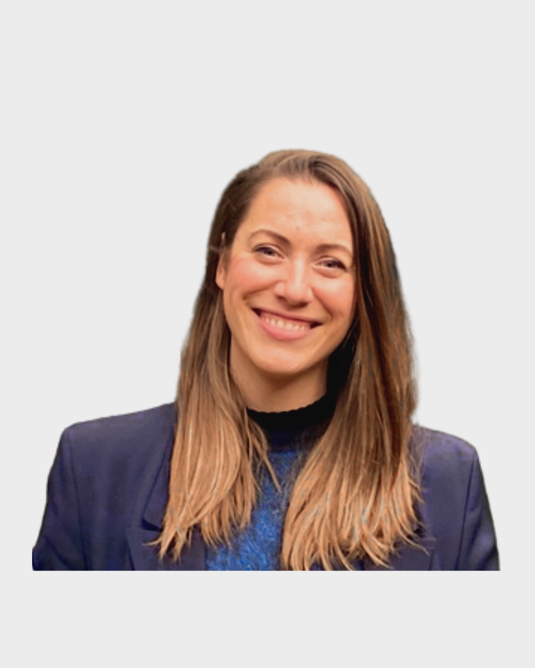 A woman with long, light brown hair smiling, wearing a dark blazer over a blue top, against a plain light gray background.