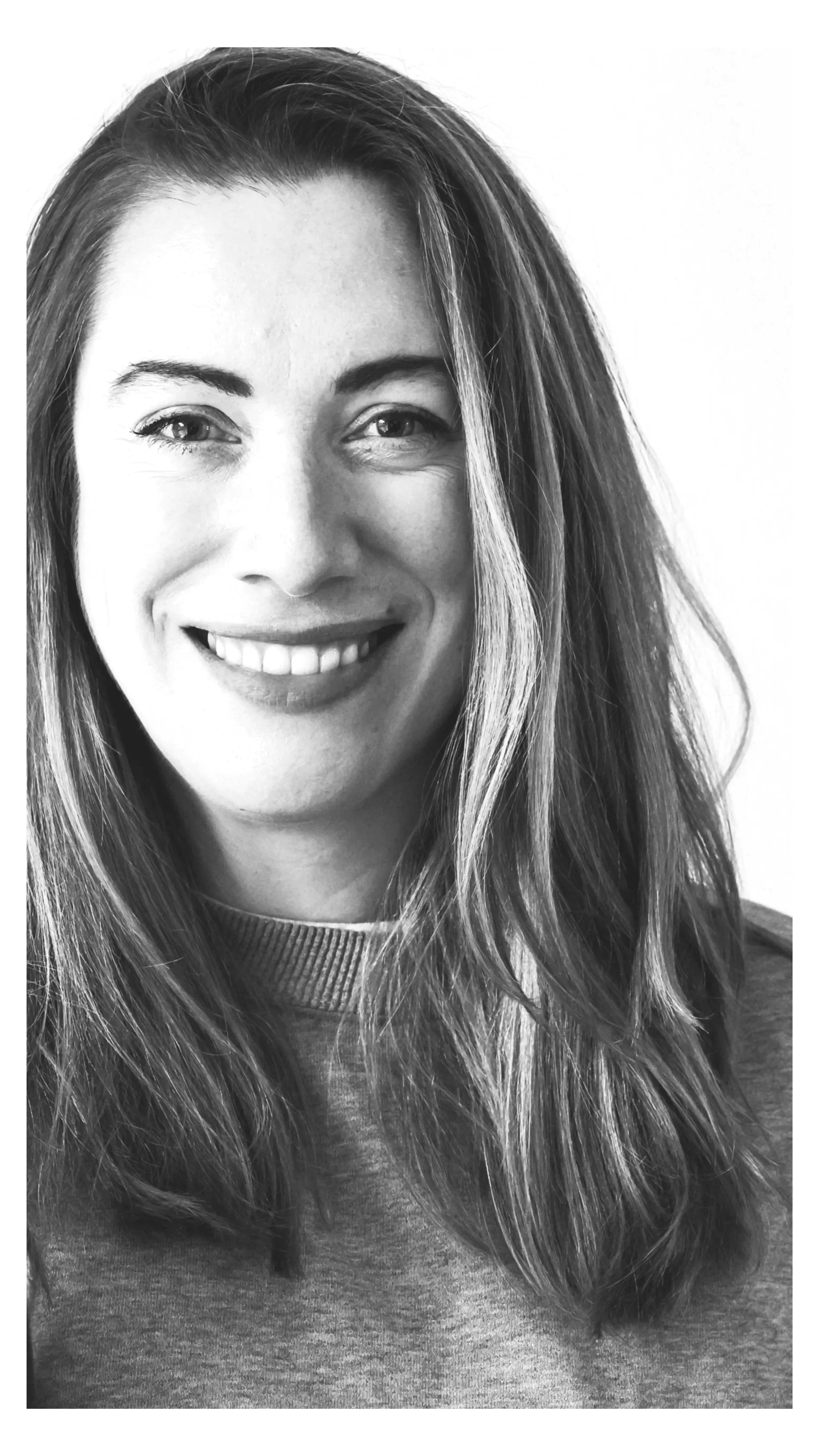 A woman with long, wavy hair smiling, black and white photo, wearing a casual top.