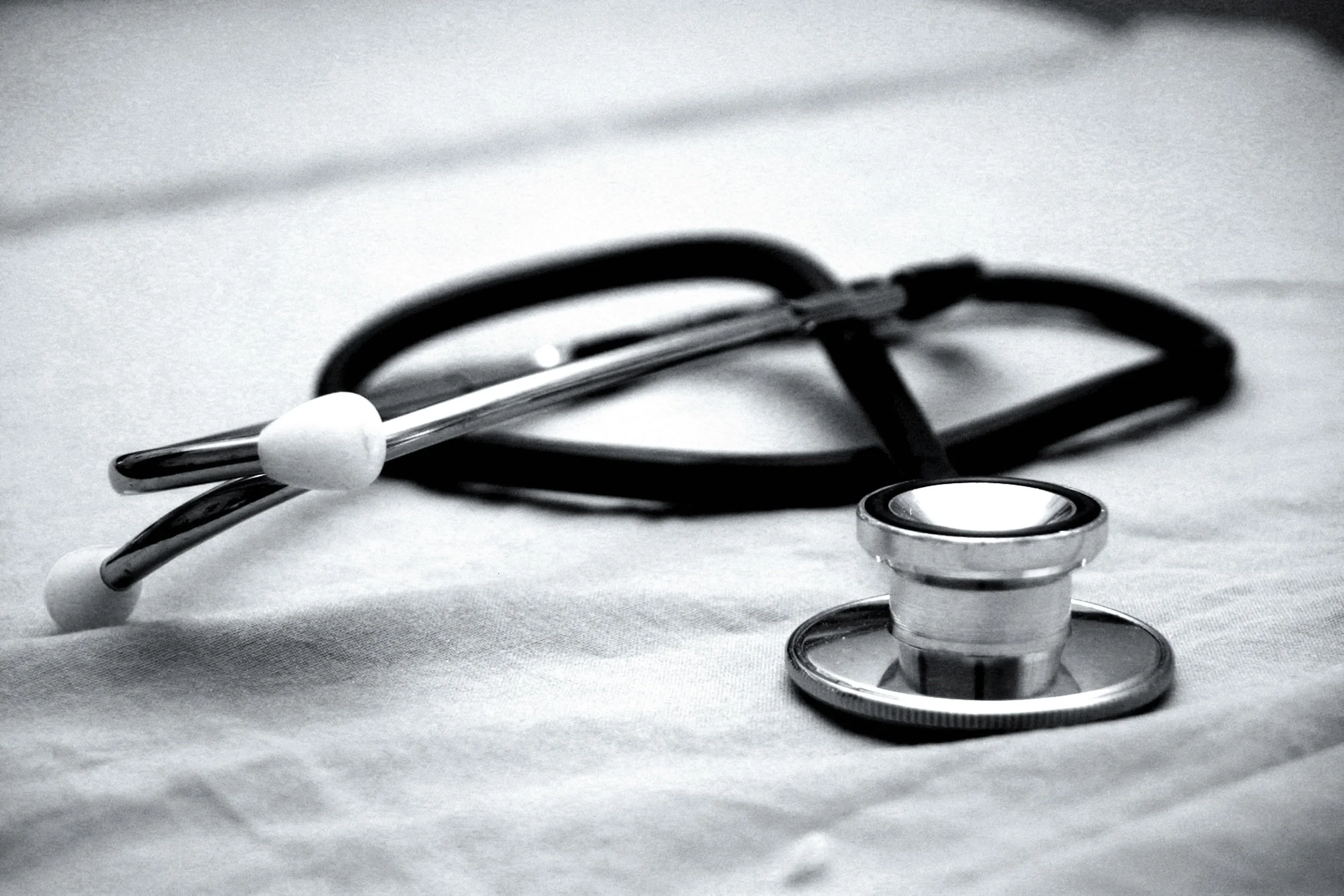 Close-up of a stethoscope intertwined with a black paperclip on a white surface.