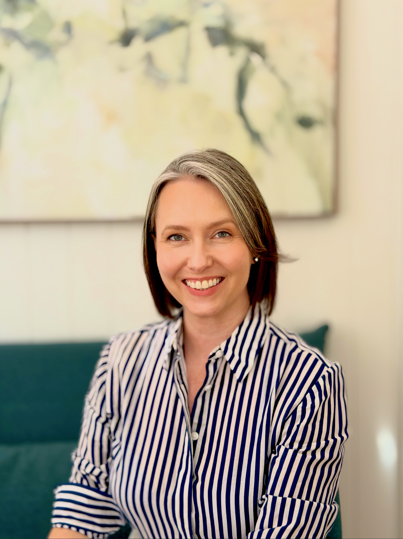 Karrie Jardine, smiling in an office with a blurred abstract painting in the background.