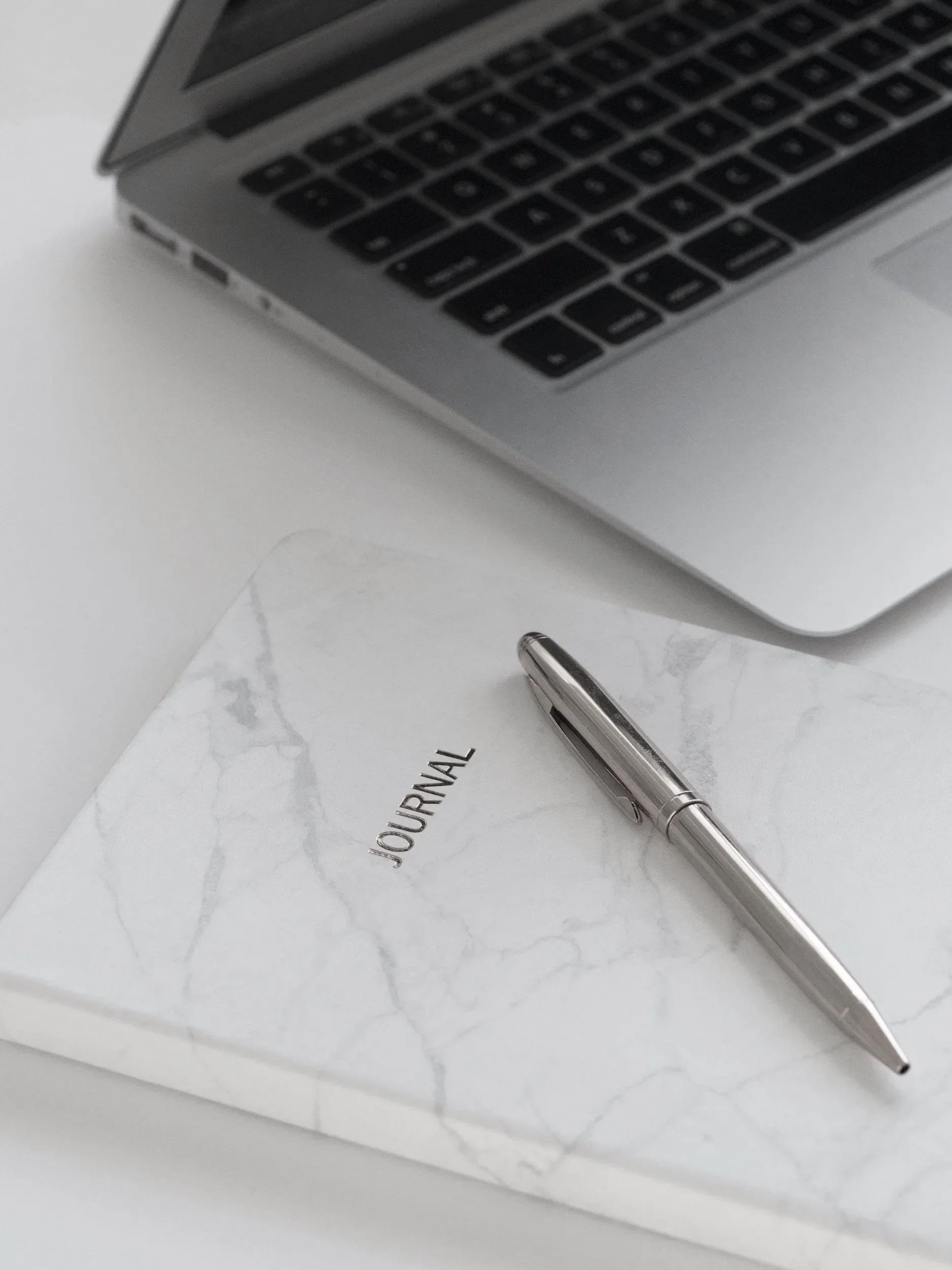 A silver pen resting on a white journal with marble pattern on the cover.