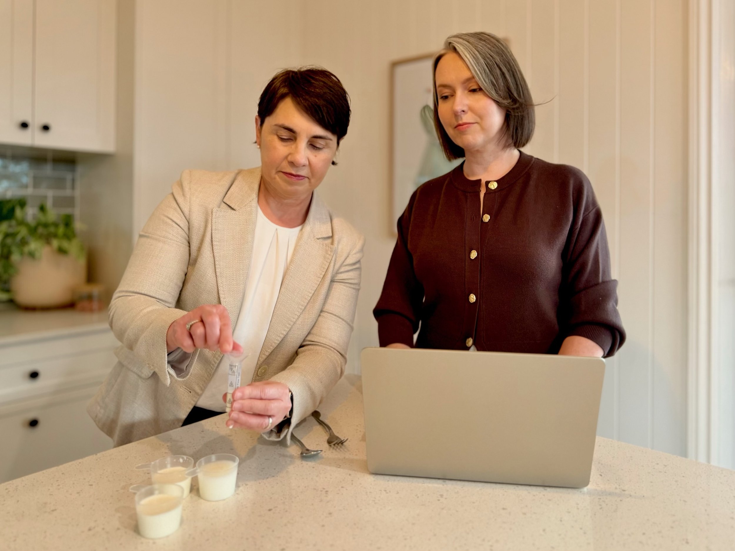 Dr Julie Cichero and Karrie Jardine demonstrating IDDSI testing of fluids in a kitchen.