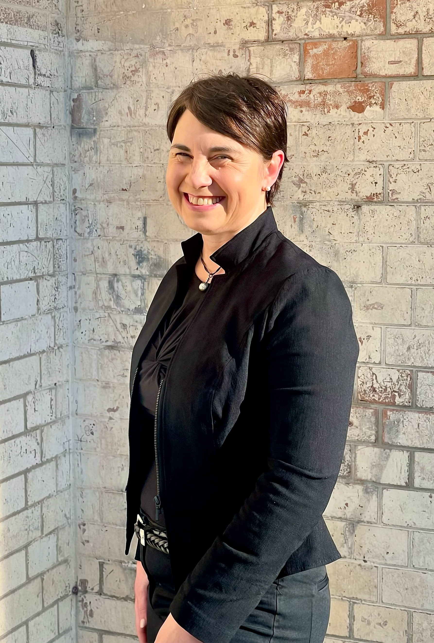 Dr Julie Cichero, smiling and standing in front of a white and red brick wall.