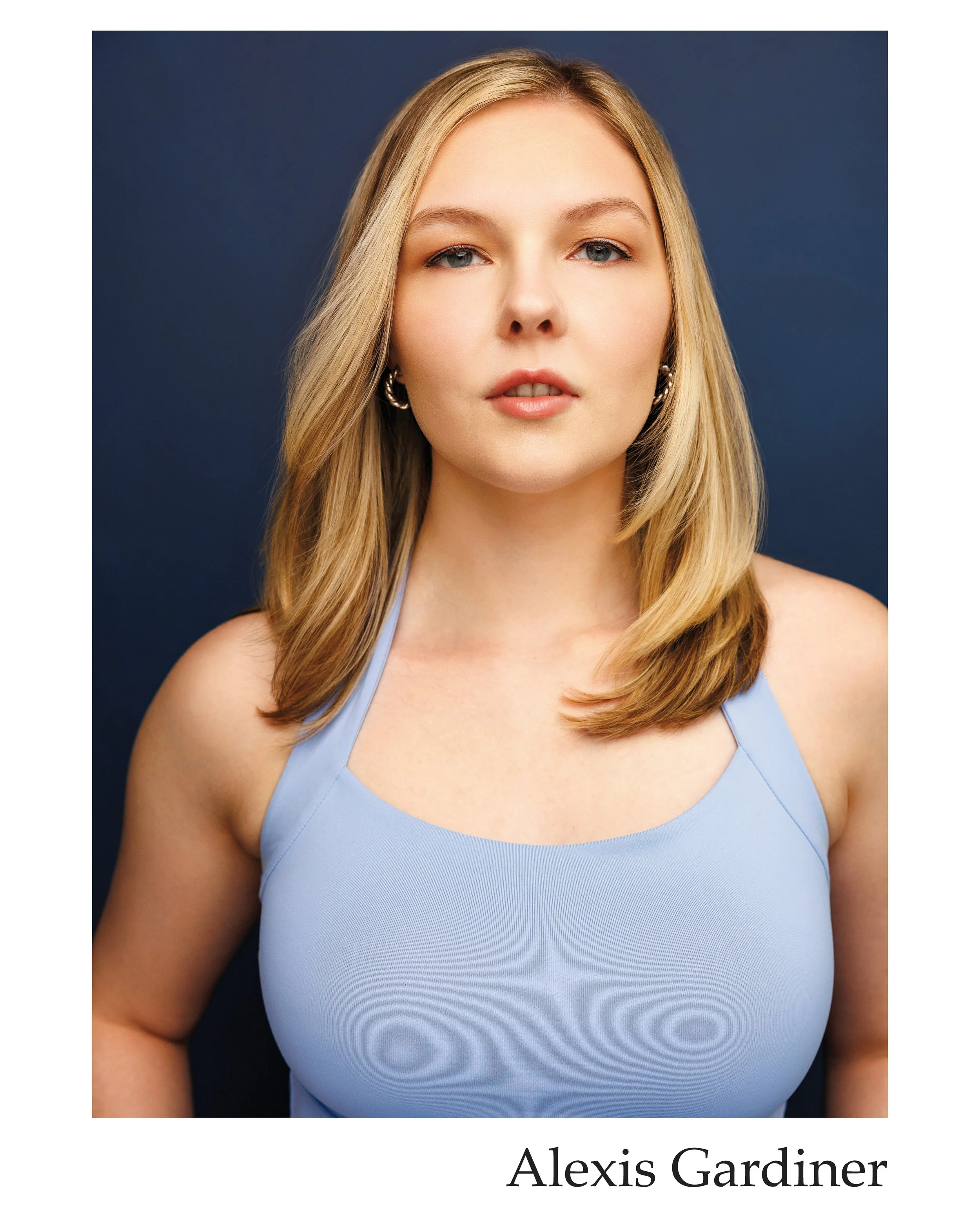 A portrait of a young woman with blonde hair wearing a light blue top, against a dark background.