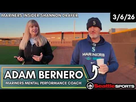 Two people, a woman and a man, standing on a baseball field during sunset. The woman is gesturing with her hands, and the man is holding a cup. They are dressed in Mariners gear. The graphic overlay shows 'Adam Bernero,' Mariners mental performance coach, and mentions 'Mariners insider Shannon Drayer' with a date of 3/6/26.