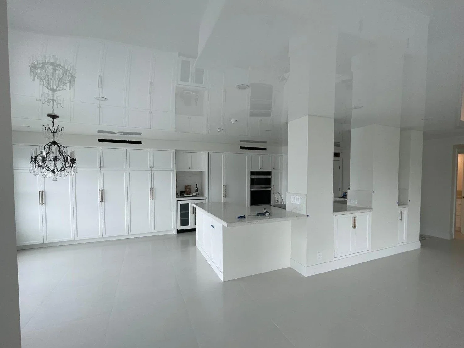 Modern kitchen with white cabinetry, marble island, built-in oven, and chandelier.