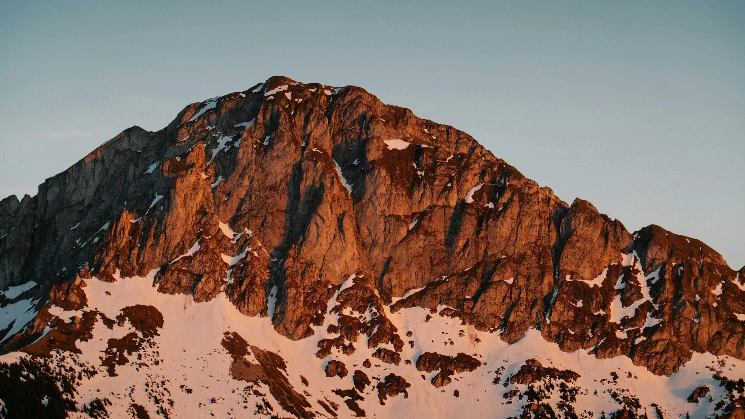 Sunset lighting on a rugged mountain peak with some snow patches.