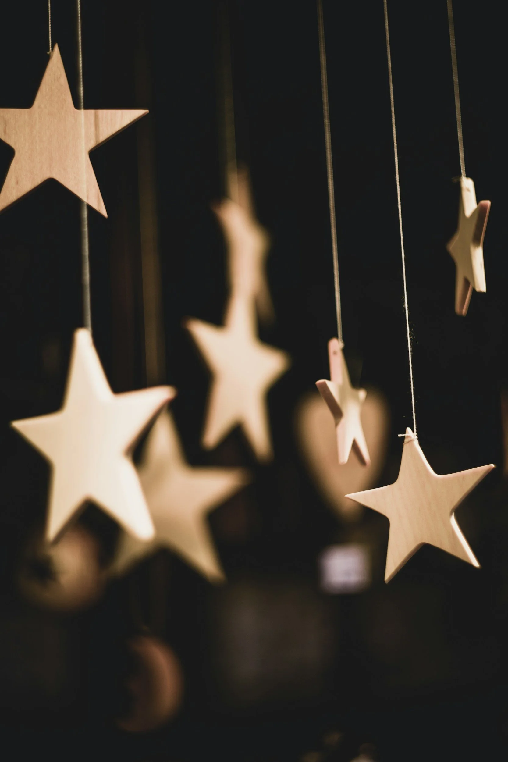 Close-up of wooden star-shaped ornaments hanging on strings against a dark background.