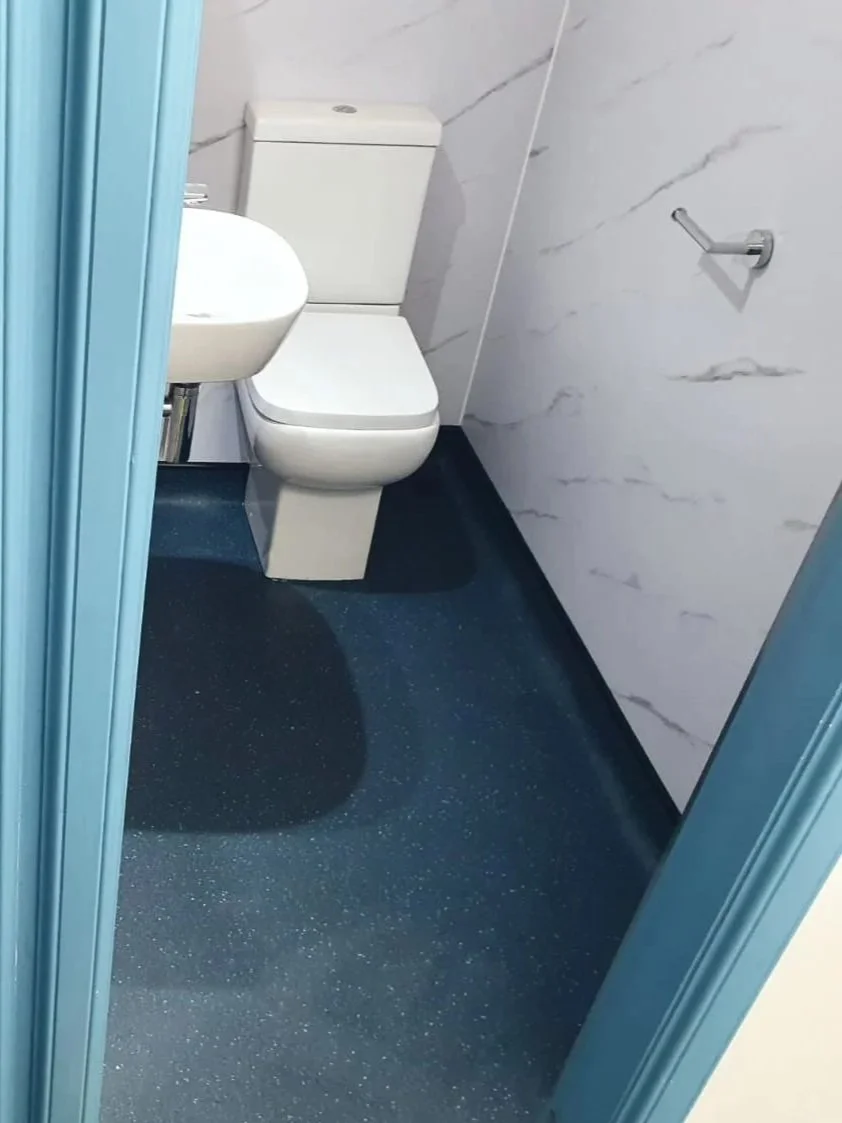 Small restroom with a white toilet, a white sink attached to the wall, blue door frame, marble-patterned wall, and dark blue speckled flooring.