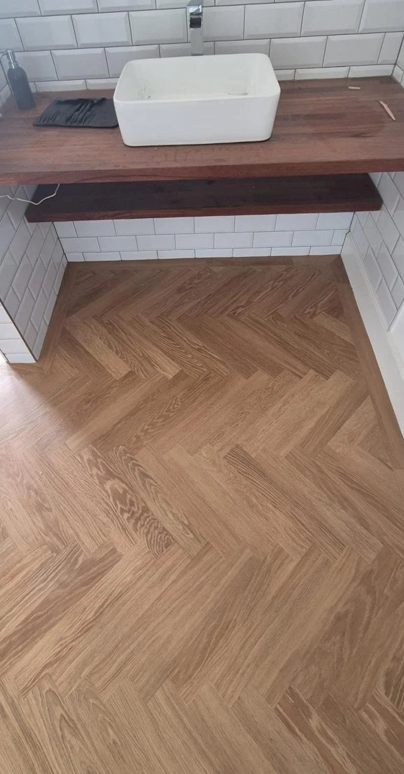 A bathroom sink on a wooden countertop with white subway tile walls and a wooden floor.