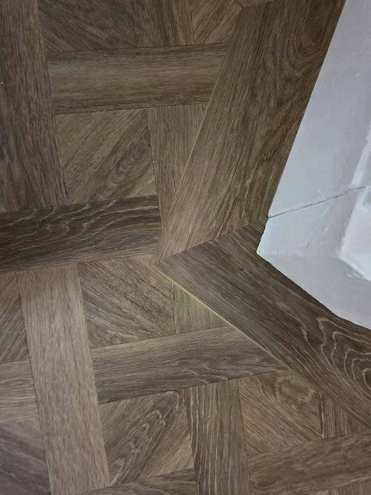 Close-up of a wooden floor with a geometric pattern near a white wall.