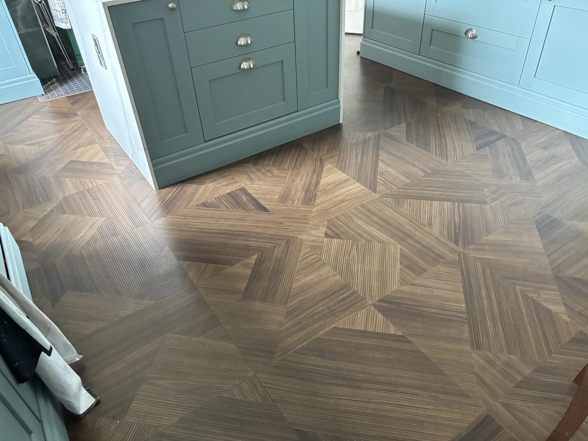 Photo of a kitchen with patterned wood flooring, teal cabinets, and a glimpse into a laundry or utility area.