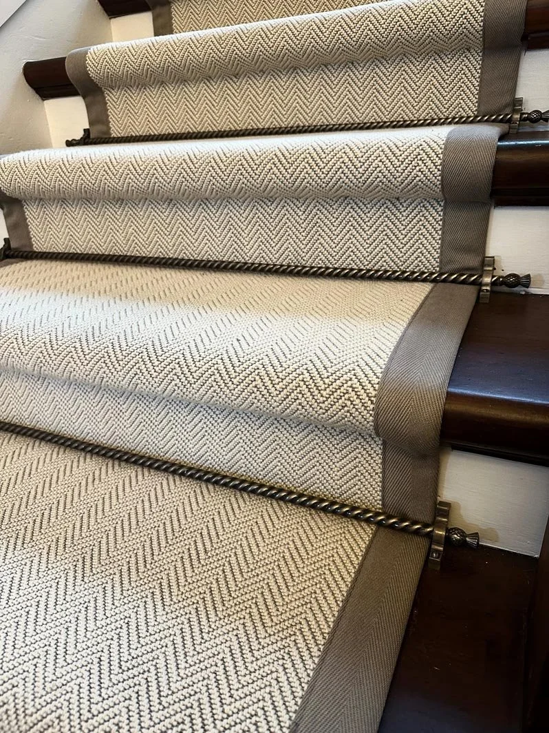Close-up of a stair with a beige and brown patterned carpet runner and dark wooden railings.