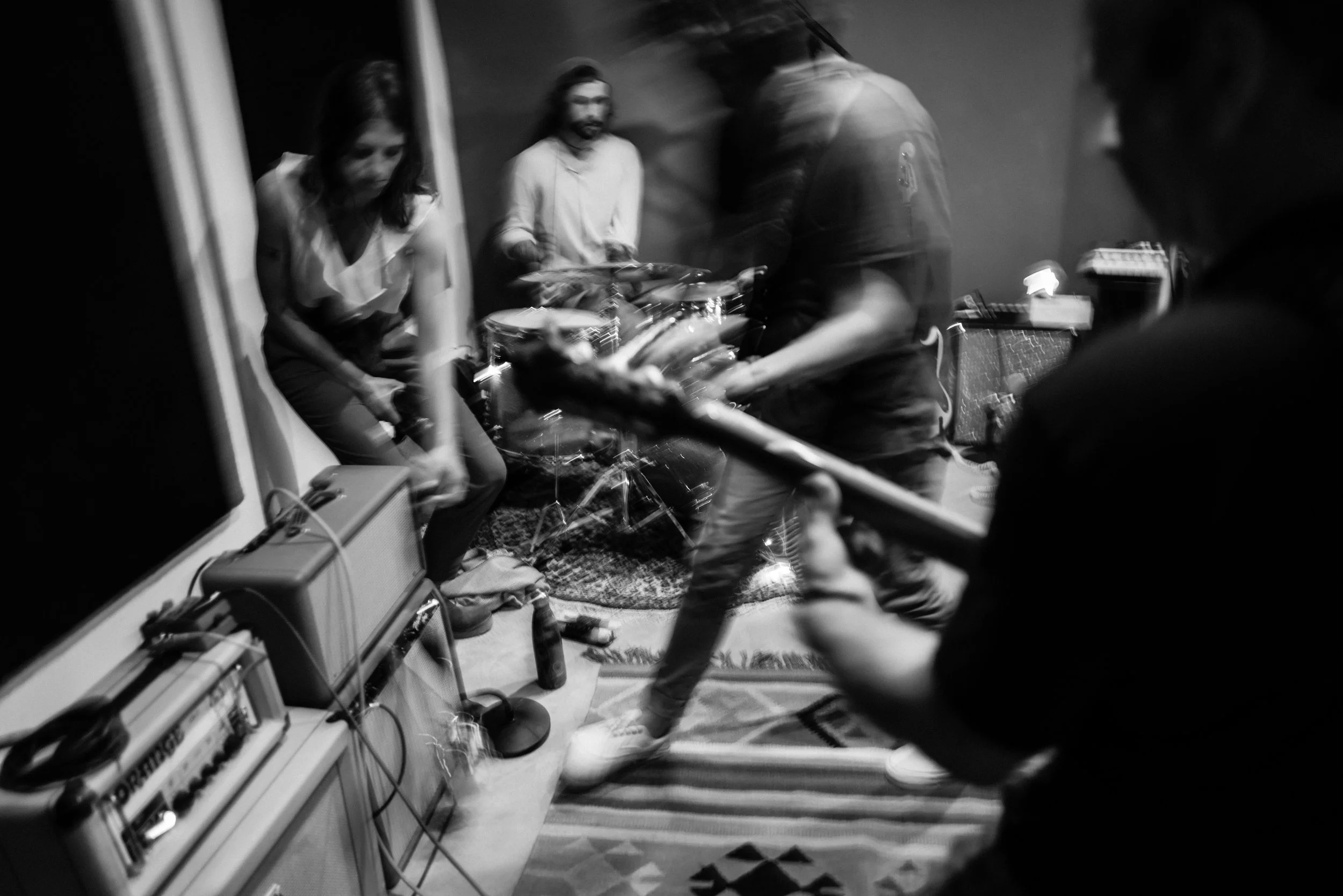Black and white photo of a band rehearsing in a studio, capturing the energy and movement of a live recording session