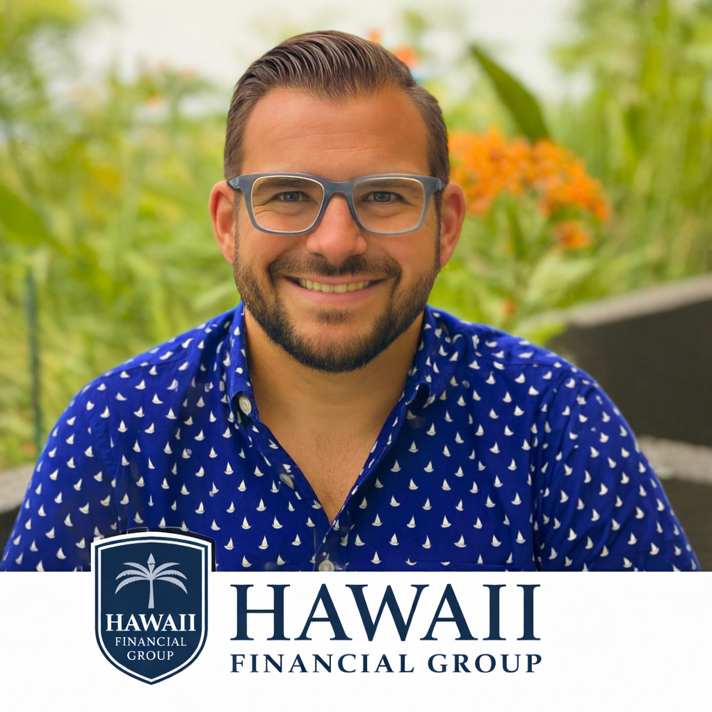 A smiling man with glasses and a beard is outdoors with green foliage and orange flowers in the background. He is wearing a blue shirt with white sailboat patterns.