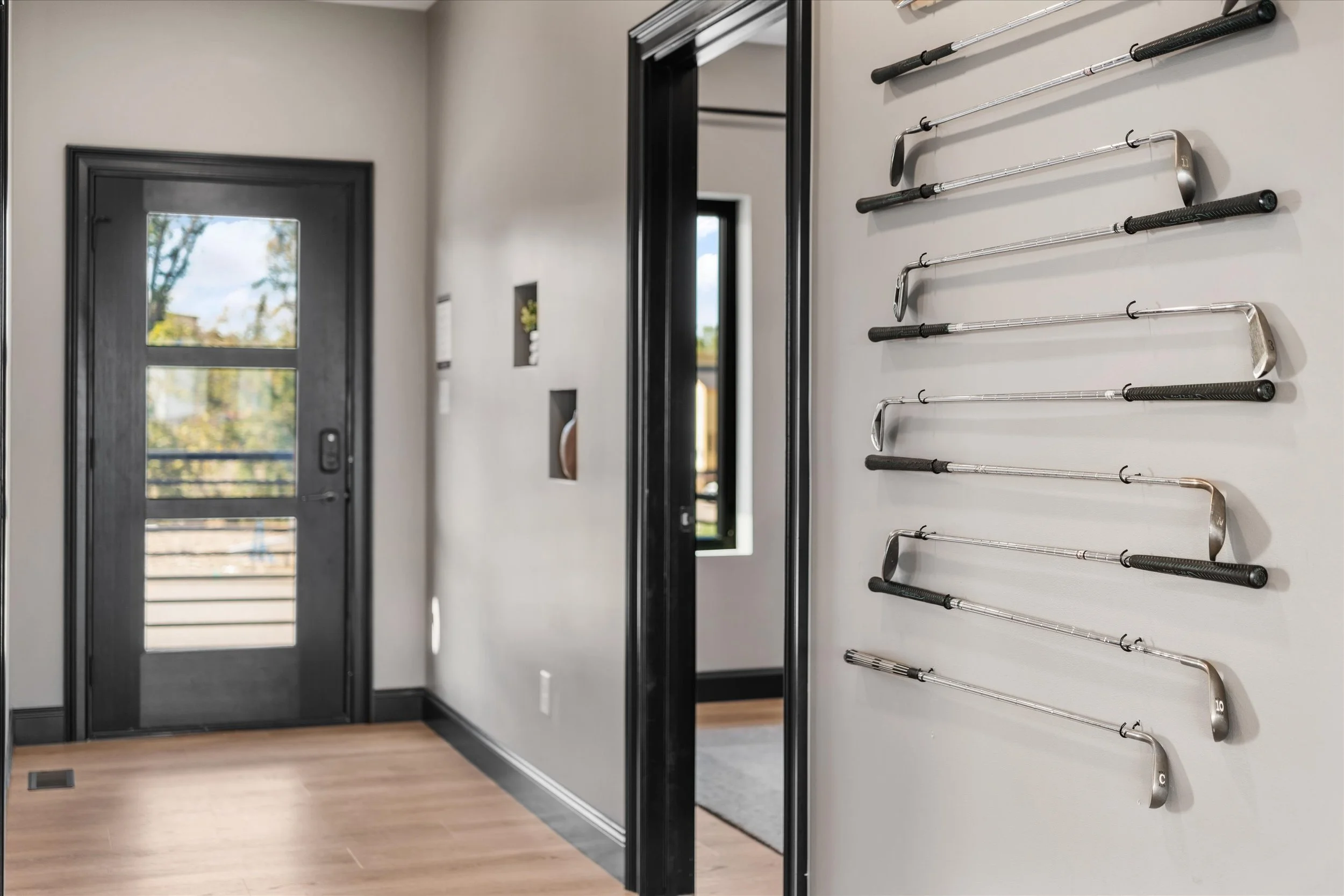 Golf clubs mounted on a beige wall in a modern room with a black door and windows